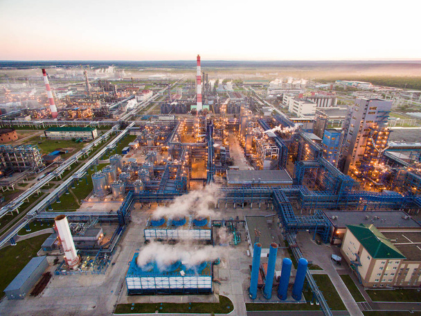 A huge oil refinery with metal structures, pipes and distillation of the complex with burning lights at dusk. Aerial view - Photo, Image
