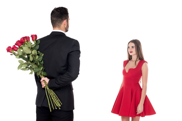 rear view of boyfriend hiding bouquet of roses from girlfriend isolated on white - 写真・画像