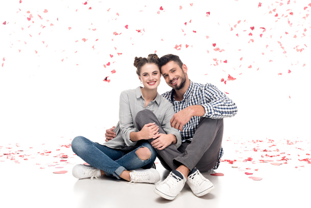 happy couple sitting under falling confetti and hugging on white, valentines day concept - Fotoğraf, Görsel