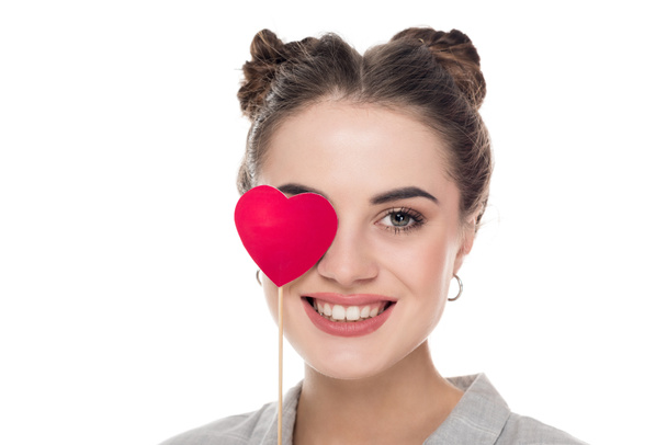 lächelndes Mädchen, das Auge mit Papierherz auf weißem Valentinstag-Konzept isoliert  - Foto, Bild