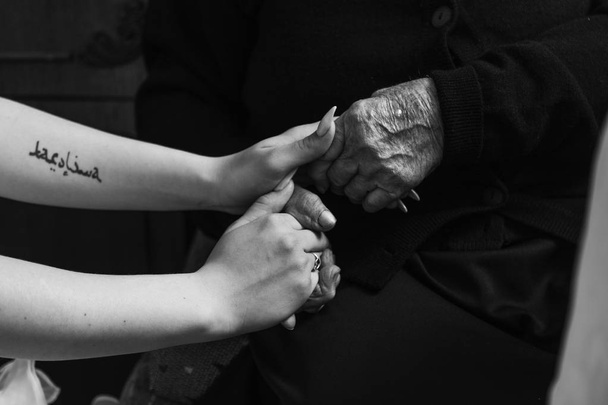 uma mulher idosa com pele enrugada segura a mão de sua filha ou neta. mãos enrugadas e mãos lisas com uma tatuagem
. - Foto, Imagem
