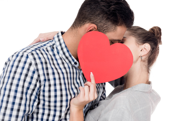 couple kissing and covering faces with paper heart isolated on white, valentines day concept - Photo, Image