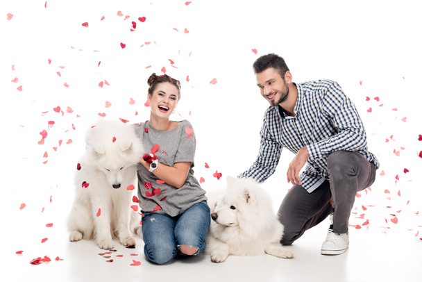 couple sitting with dogs under falling confetti on white, valentines day concept - Foto, Imagen