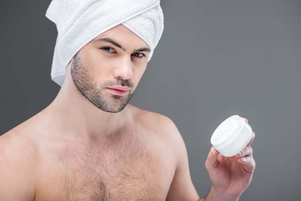 bearded man in towel holding face cream, isolated on grey - 写真・画像