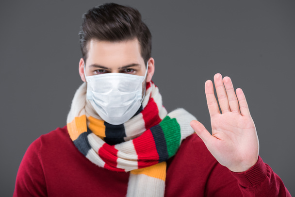 больной человек в теплом шарфе и медицинской маске со знаком "стоп", изолированный на сером
 - Фото, изображение