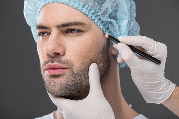 doctor drawing lines for facelifting on man, isolated on grey - Photo, Image