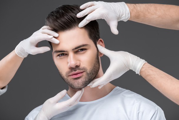 bearded handsome man and doctors hands, isolated on grey, skin care concept - Photo, Image