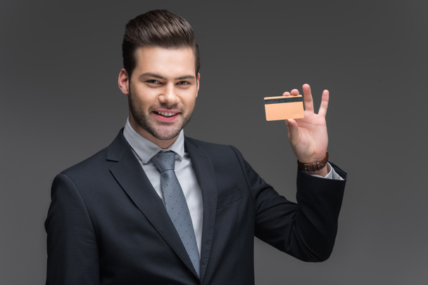 handsome cheerful businessman holding golden credit card, isolated on grey - Foto, Imagem