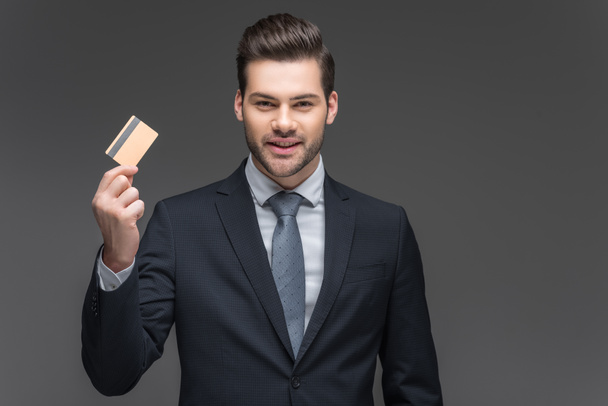 cheerful businessman holding credit card, isolated on grey - Foto, afbeelding