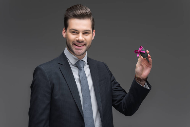 smiling businessman holding car key, isolated on grey - Foto, afbeelding