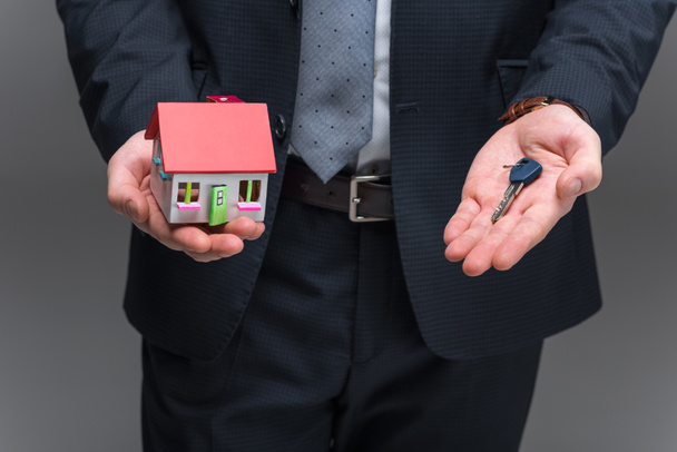 cropped view of realtor holding house model and key, isolated on grey - Fotografie, Obrázek