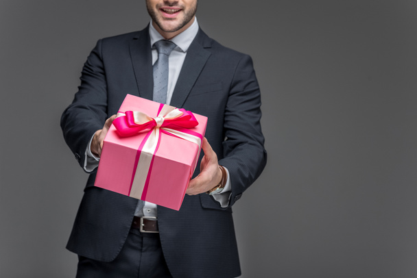 abgeschnittene Ansicht eines Mannes im Anzug mit Geschenkbox, isoliert auf grau - Foto, Bild