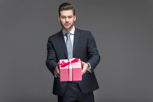 handsome man in suit holding present, isolated on grey - Fotó, kép