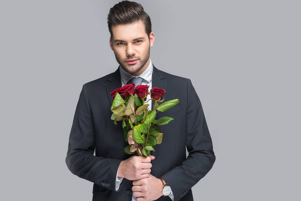 elegant man holding bouquet of red roses, isolated on grey - 写真・画像