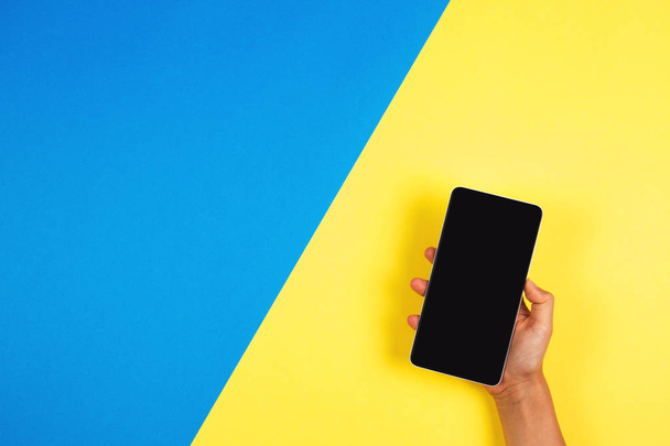 Hand holding the phone on blue and yellow background - Fotografie, Obrázek