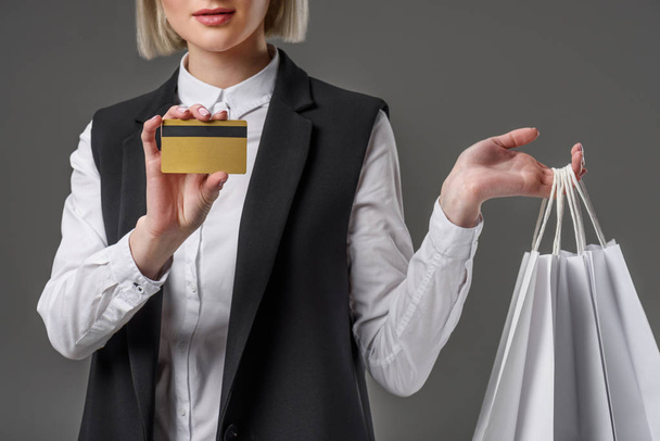 Schnappschuss einer stilvollen Frau mit Kreditkarte und Einkaufstaschen isoliert auf grau - Foto, Bild