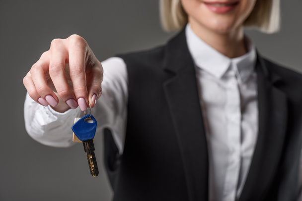 cropped shot of businesswoman showing keys from house in hand isolated on grey - Foto, Imagem