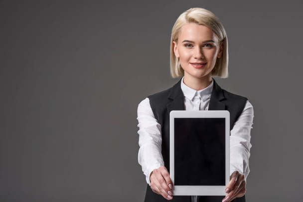 портрет улыбающейся женщины, показывающей планшет с чистым экраном, изолированным на сером
 - Фото, изображение