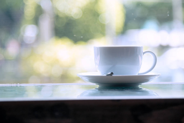 Fehér csésze kávé asztal mellett ablak kívül a bokeh forgalomba hozatala  - Fotó, kép