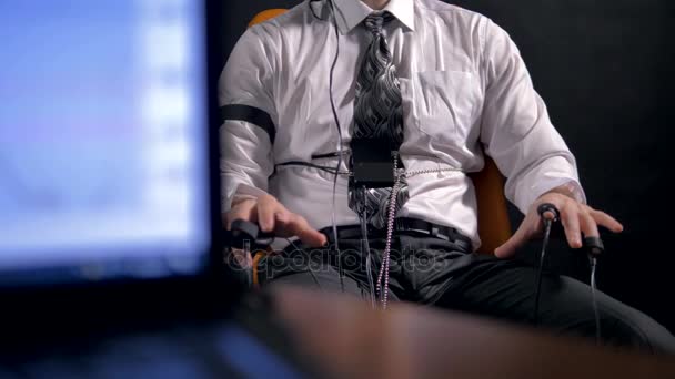 座っている男の横にうそ発見器によるデータをコンピューターでモニターします。. - 映像、動画