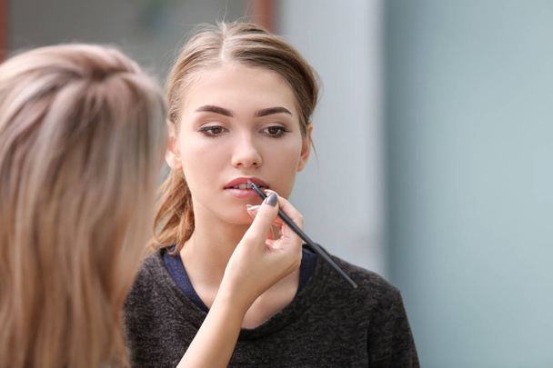 Professional artist creating makeup for beautiful model on blurred background - Valokuva, kuva