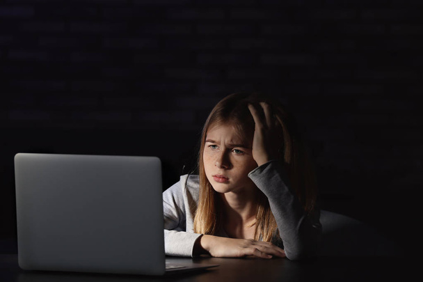 Sad teenage girl sitting near laptop in dark room - 写真・画像