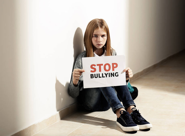 Sad teenage girl holding "Stop bullying" sign indoors - Foto, Bild