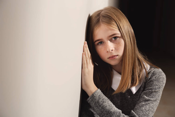 Sad teenage girl leaning against wall indoors - Фото, изображение