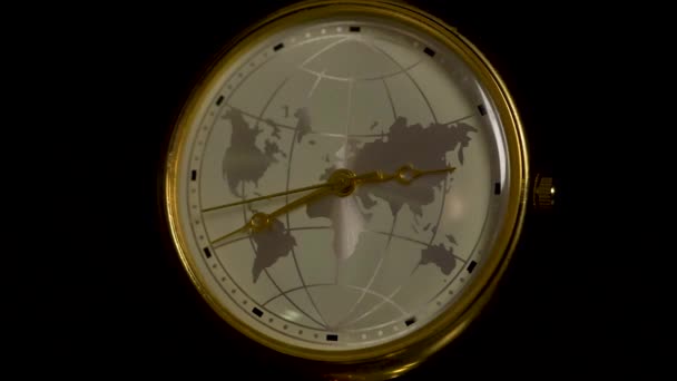 Ρολόι με μια εικόνα του πλανήτη γη σε έναν ξύλινο πίνακα που απομονώνονται σε μαύρο φόντο. Λεπτομέρεια από ένα ρετρό ρολόι με timezones και αεροπλάνο. Γη ρολόι με θολή φως στο σκοτεινό δωμάτιο. Concept ώρα της γης - Πλάνα, βίντεο