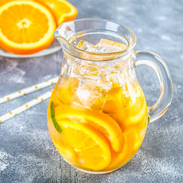 Orange detox water in a pitcher on a gray concrete background. Healthy food, drinks. - Foto, imagen