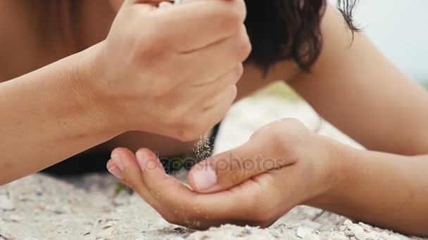 Женские руки высыпают песок с раковинами на пляж Черного моря летом в сло-мо Мечтательный крупный план рук молодой женщины, берущей горсти песка и просеивающей его на побережье Черного моря летом в замедленной съемке
. - Кадры, видео