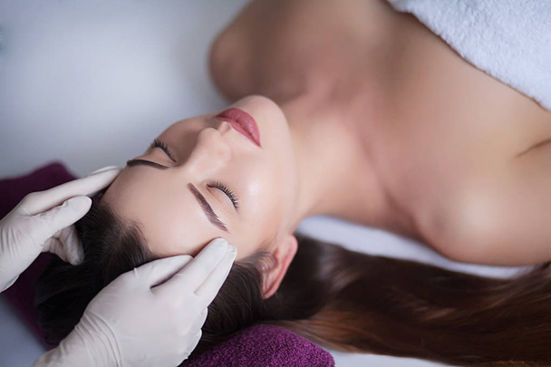 Красива молода жінка розслабляється з масажем обличчя в косметичному спа-центрі
 - Фото, зображення