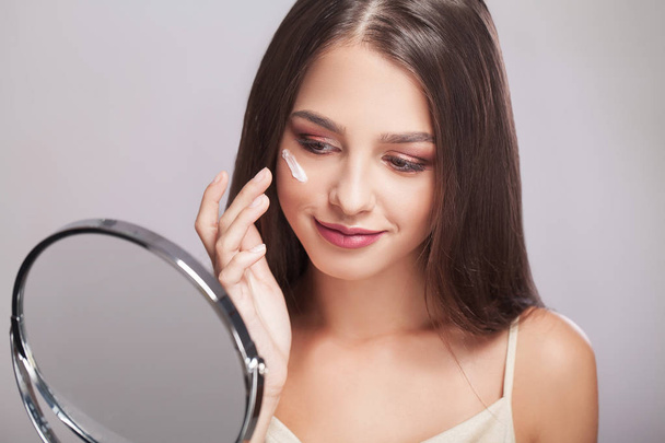 Mujer con cara sana aplicando crema cosmética debajo de los ojos
 - Foto, Imagen