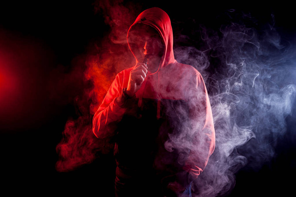 Mężczyzna pali elektroniczny papieros na ciemnym tle - Zdjęcie, obraz
