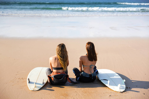 Two beautiful female friends sitting at beach with surfboards - Φωτογραφία, εικόνα