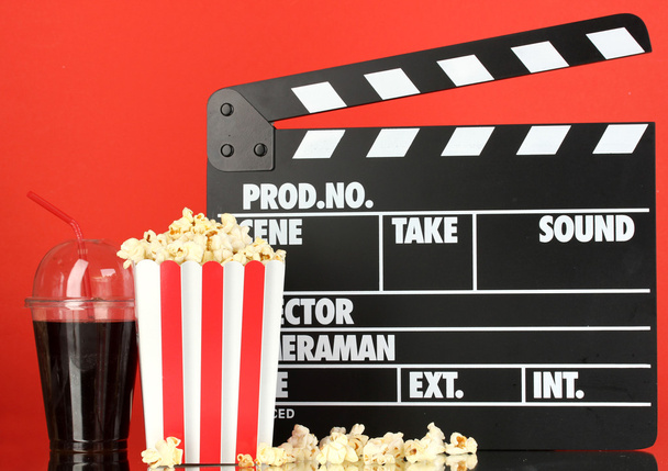 Movie clapperboard, cola and popcorn on red background - Фото, изображение