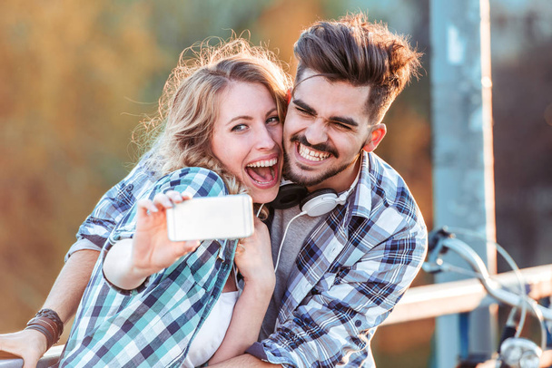Preciosa pareja joven tomando foto selfie con teléfono inteligente en el parque
. - Foto, Imagen