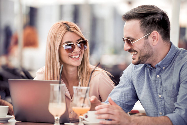 Красива молода пара використовує ноутбук, розмовляє і посміхається, сидячи в кафе
 - Фото, зображення