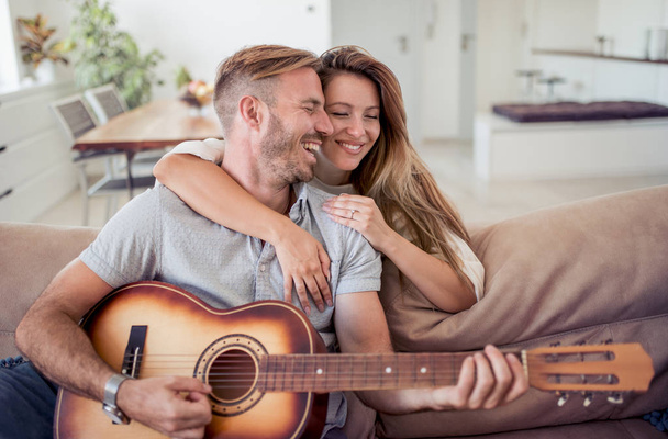 Man playing guitar in living room and woman listening, romantic moments. - Φωτογραφία, εικόνα