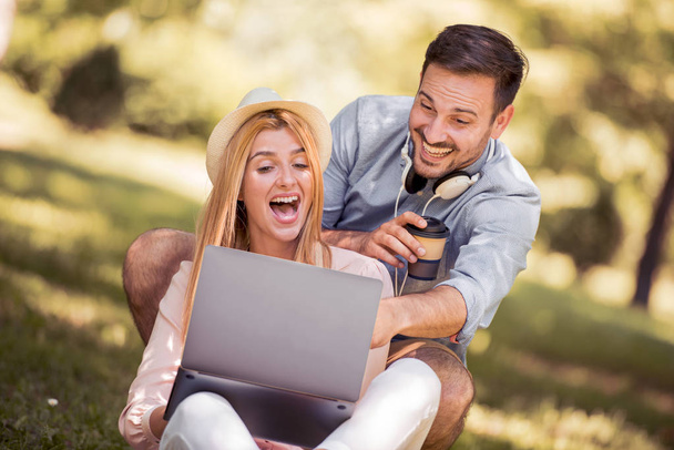 Young couple sit on the ground in the park and look into the laptop. - Photo, Image