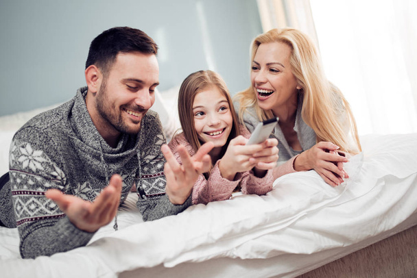 Szczęśliwa młoda rodzina. Matka, ojciec i córka zabawy grając w łóżku - Zdjęcie, obraz