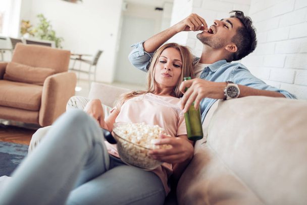Молода пара розслабляється на дивані і їсть попкорн
. - Фото, зображення