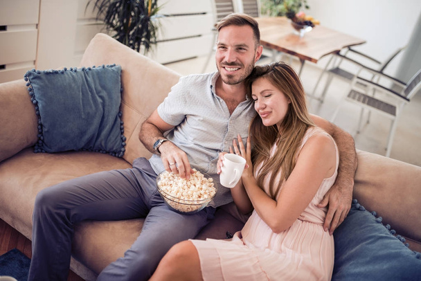 Adult lovely couple sitting on sofa and eating popcorn while watching movie. - Fotoğraf, Görsel