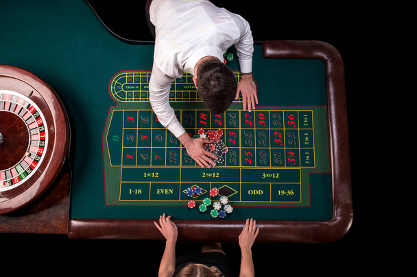 Man croupier and woman playing roulette at the table in the casino. Top view at a roulette green table with a tape measure. - Photo, Image