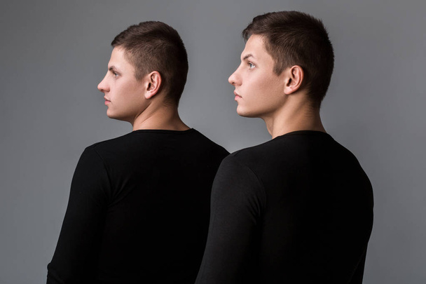 The two twin brother stand with their backs on the gray backgrou - Foto, immagini