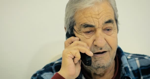 Grootvader van tweeëntachtig jaar gesprek met zijn vriend aan de telefoon zitten op een stoel in de kamer. - Video