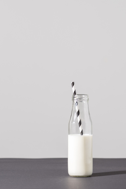 glazen flesje met melk en gestreepte drinken stro op grijs - Foto, afbeelding