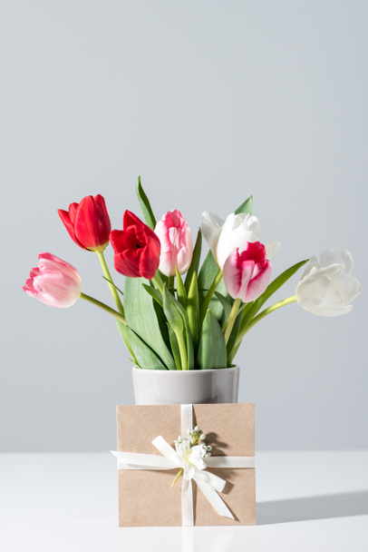 vergrote weergave van mooie bloeiende tulp bloemen in vaas en envelop op grijs - Foto, afbeelding