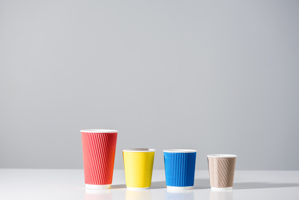 різні кольорові паперові чашки в ряд на сірому
  - Фото, зображення
