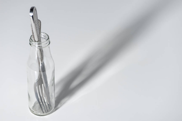 vergrote weergave van de vork en mes in glazen fles met schaduw op grijs - Foto, afbeelding